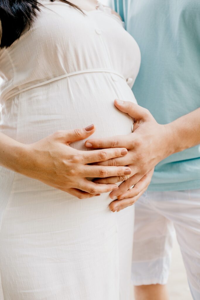 pregnant lady in white linen caressing belly with partner is an example of womanhood