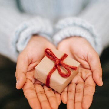open palms holding tiny brown paper gift with red string