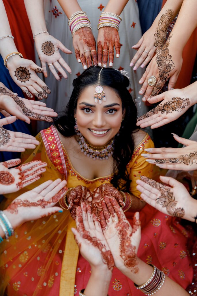 woman in center of circle of hands with henna designs reflects the village of traditional womanhood