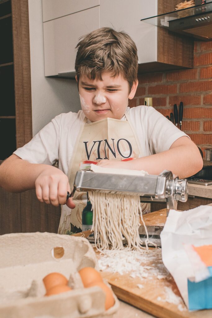 funny image of boy speckled with flour attempting to make pasta represents a traditional self-sufficient kitchen skill