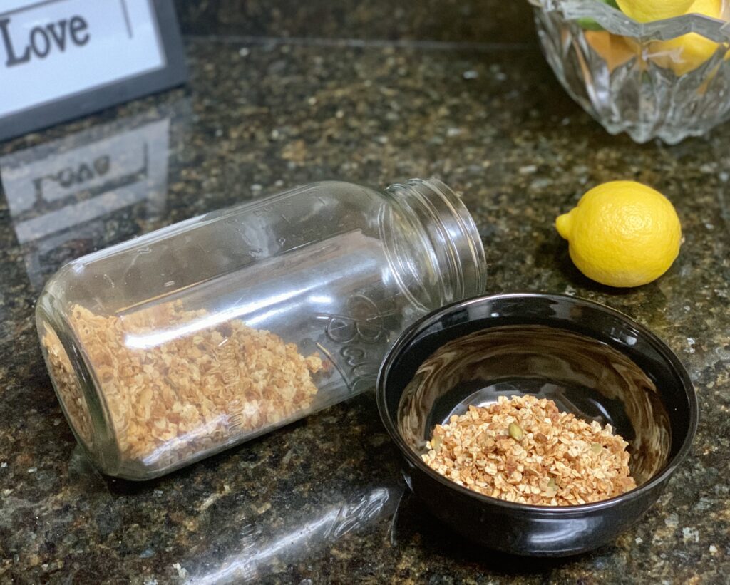 Homemade granola in a bowl on a counter with a large jar half filled with granola and a lemon