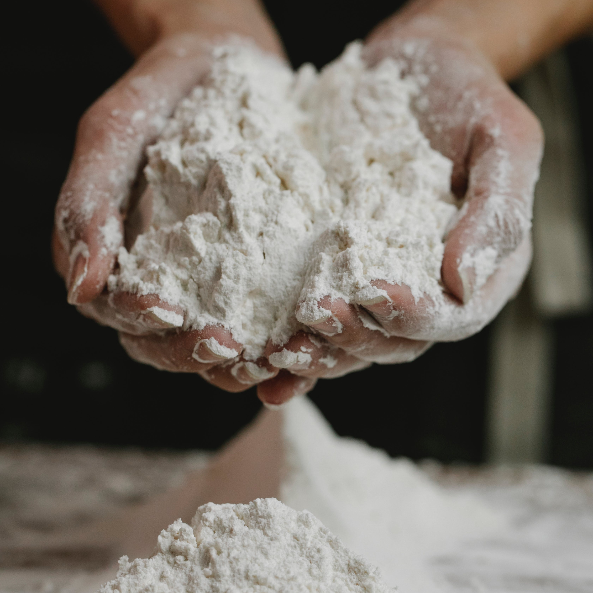 brown hands with palms open holding ground flour, one of the essential pantry staples in a self-sufficient kitchen
