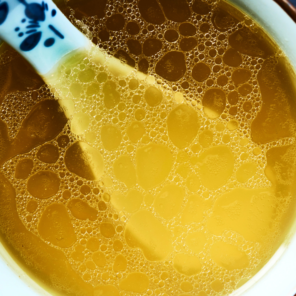 golden yellow broth with fat droplets on the surface in a white glass bowl with a white Asian soup spoon