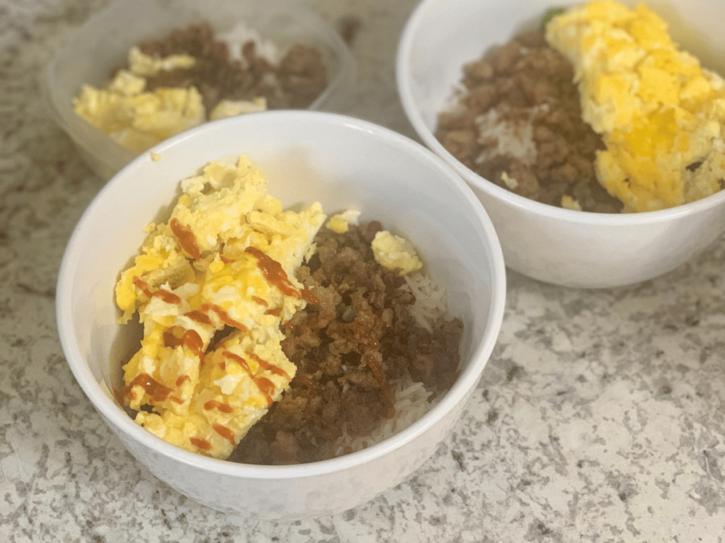 3 bowls filled with homemade food - browned meat, golden yellow eggs and rice, one with red sauce all sitting on the kitchen counter