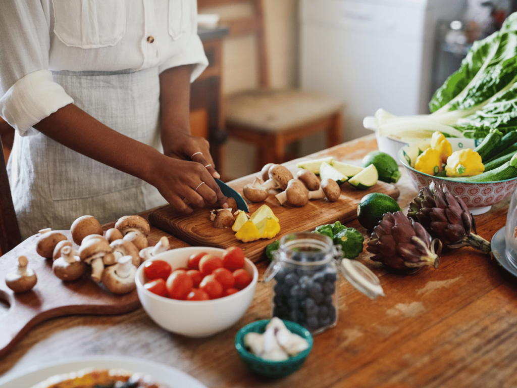 brown girl arms cutting produce on a wooden cutting board on a wooden table filled with a variety of colorful produce meal planning for a month