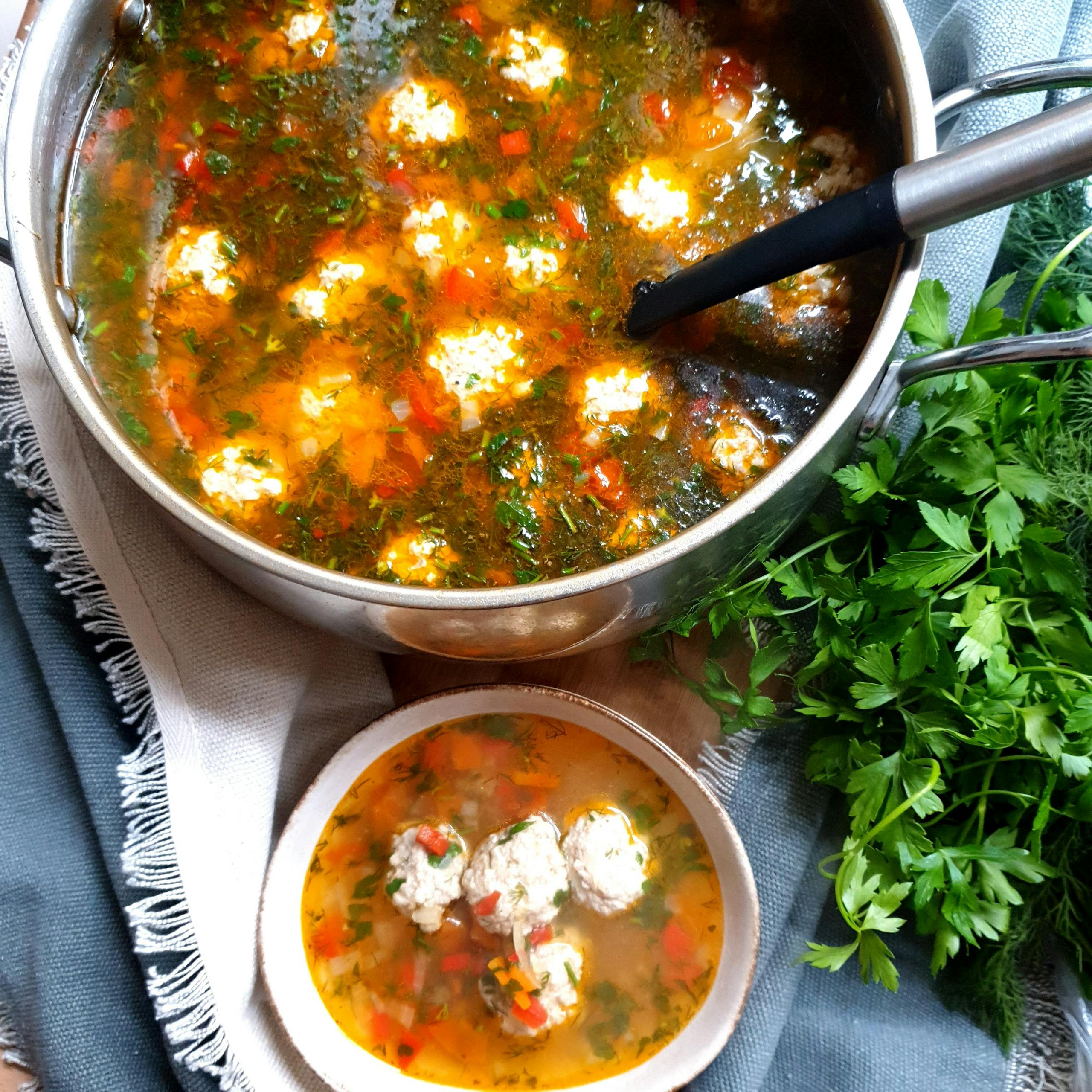 Delicious homemade meatball soup with fresh parsley in a stainless steel pot.